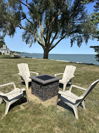 A fire pit surrounded by three chairs on a lawn.